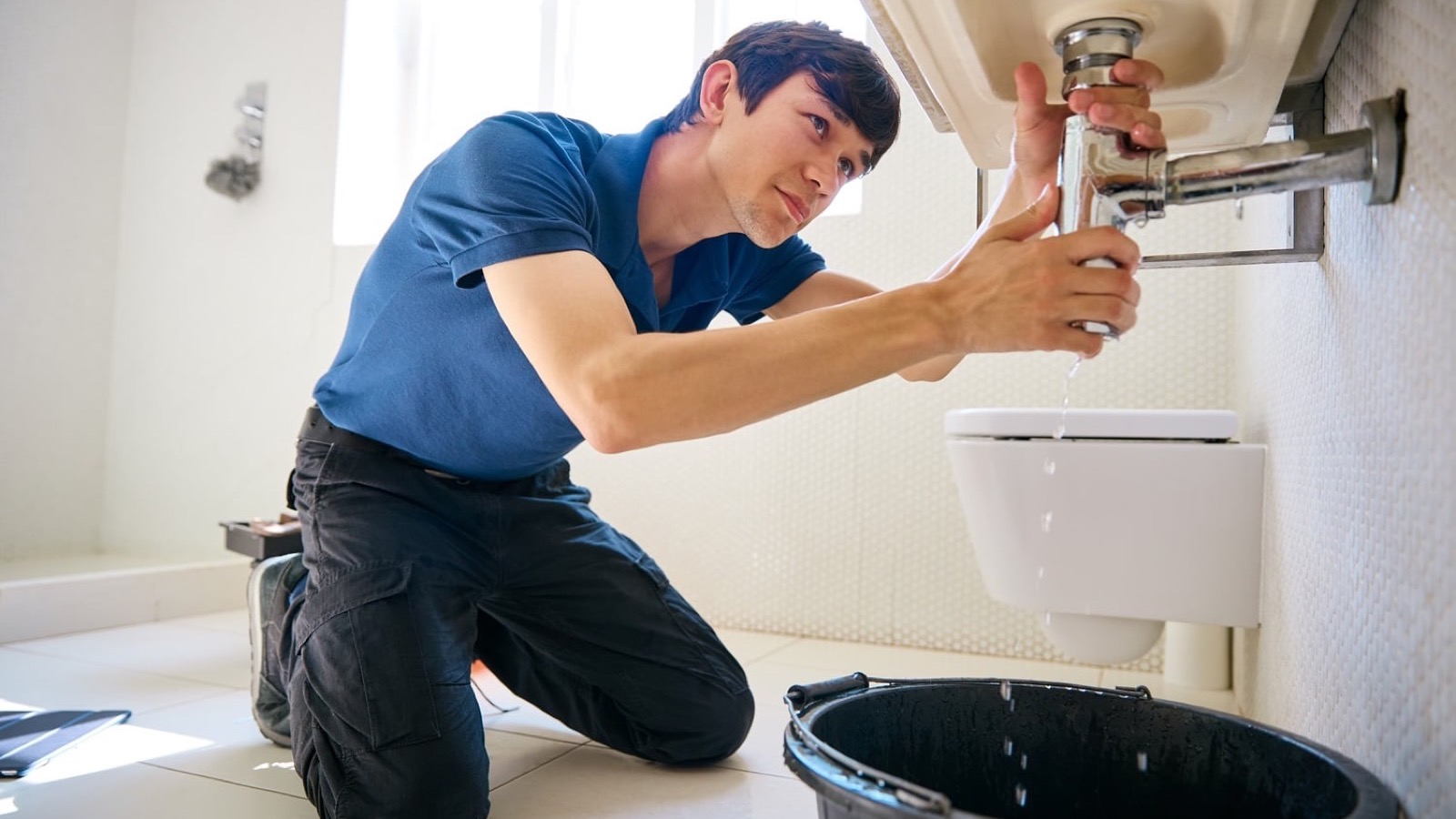 Plumber inspecting pipes under a kitchen sink in a Mesa home